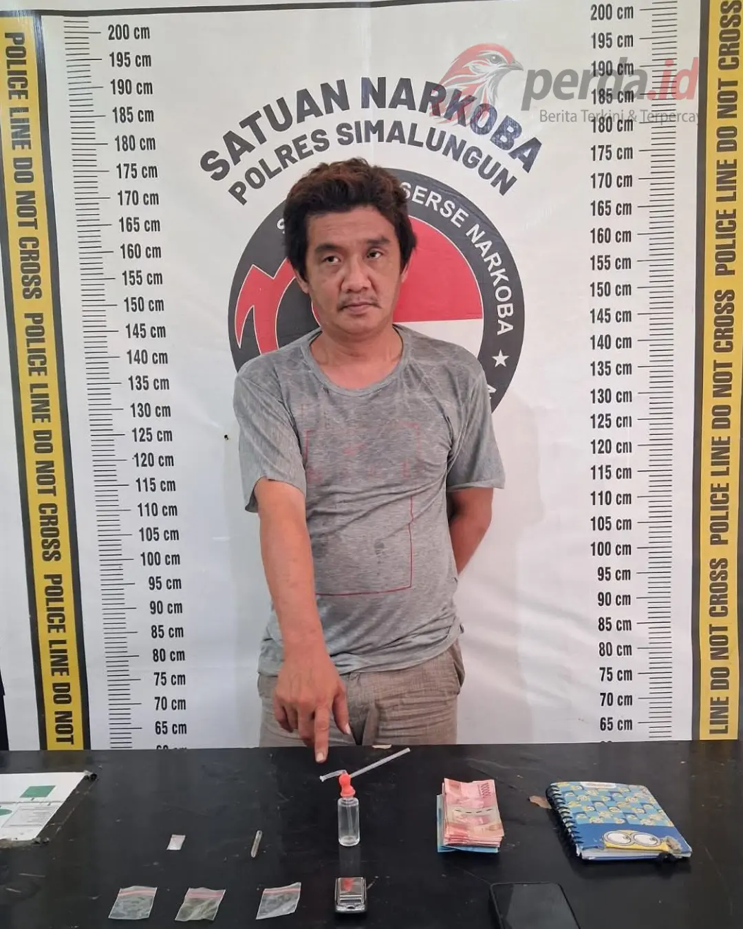 Foto tersangka Y, pria 45 tahun berpakaian abu-abu, berdiri di depan latar belakang Satresnarkoba Polres Simalungun dengan latar papan ukur tinggi badan.